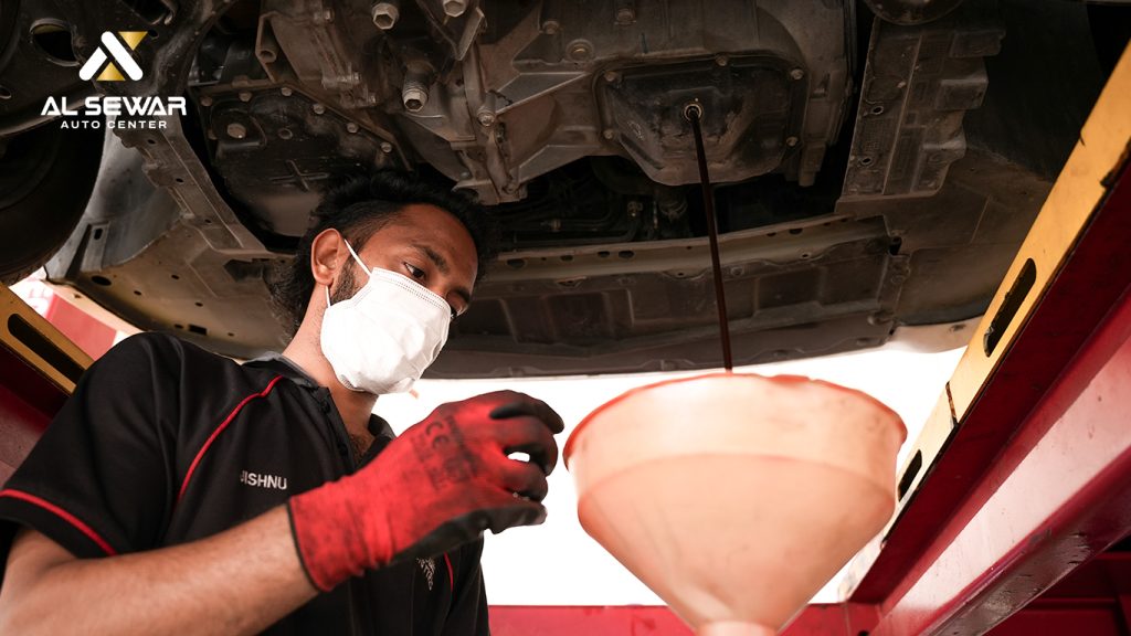 Mechanic performing oil change service at Al Sewar automotive center – close-up of car engine and technician’s hands replacing oil