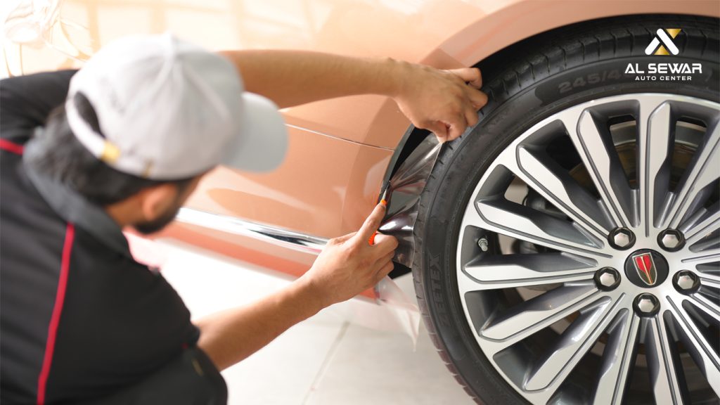 Technician applying Paint Protection Film (PPF) to a car fender at Al Sewar Auto Center in the UAE