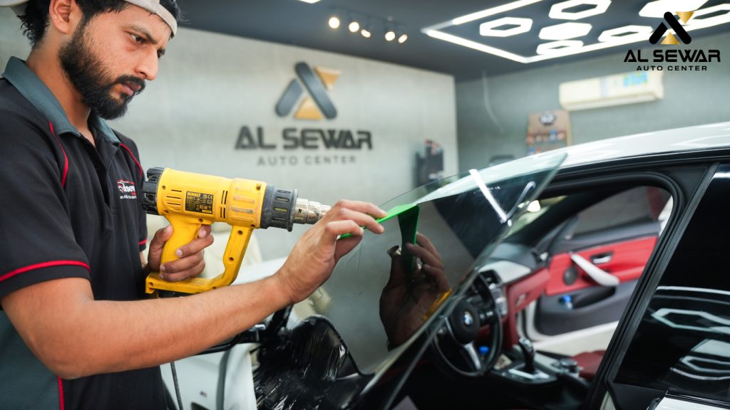 Technician applying window tint film on a car door using a heat gun at Al Sewar Auto Center in Dubai, enhancing UV protection and privacy.
