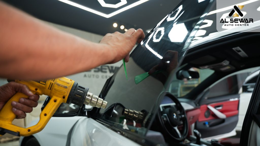 “Technician applying protective window film to a car hood at Al Sewar Auto Center in Sharjah Kalba.”